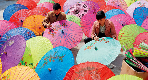 Former migrant workers drawing on the umbrella surface at a village traditional paper umbrella factory of Wuyuan County, Jiangxi Province